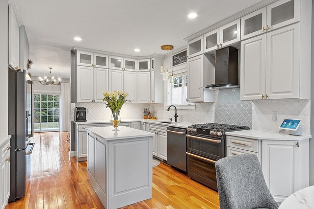 kitchen featuring wall chimney range hood, light countertops, a sink, stainless steel appliances, and a notable chandelier