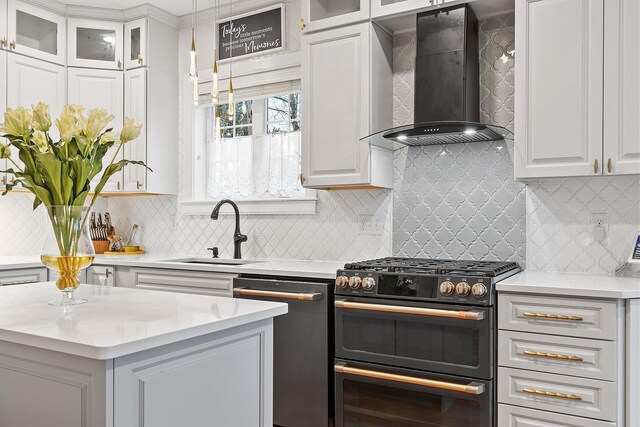 kitchen with dishwasher, a sink, wall chimney range hood, light countertops, and range with two ovens