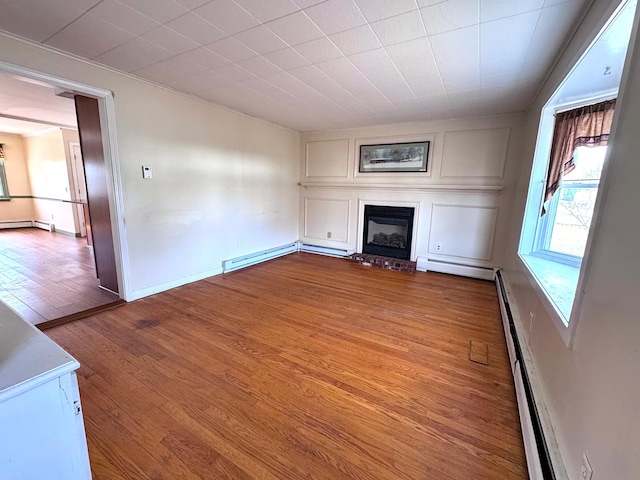 unfurnished living room with crown molding, a large fireplace, wood finished floors, a baseboard heating unit, and a baseboard radiator