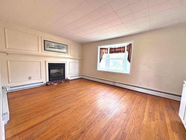 unfurnished living room with baseboard heating, light wood-style floors, and a glass covered fireplace