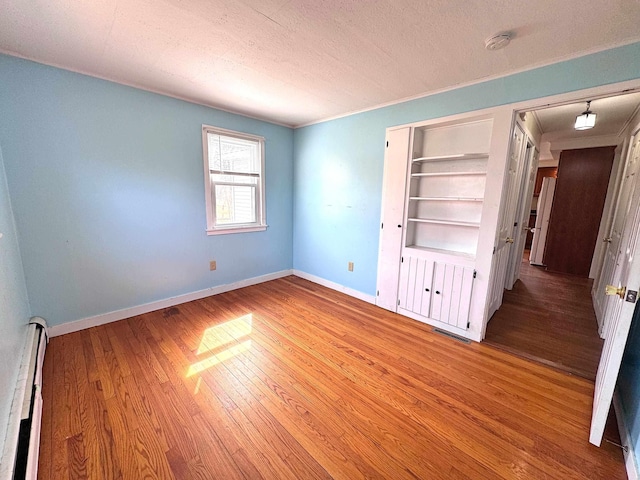 unfurnished bedroom with a textured ceiling, visible vents, wood finished floors, a baseboard heating unit, and baseboards