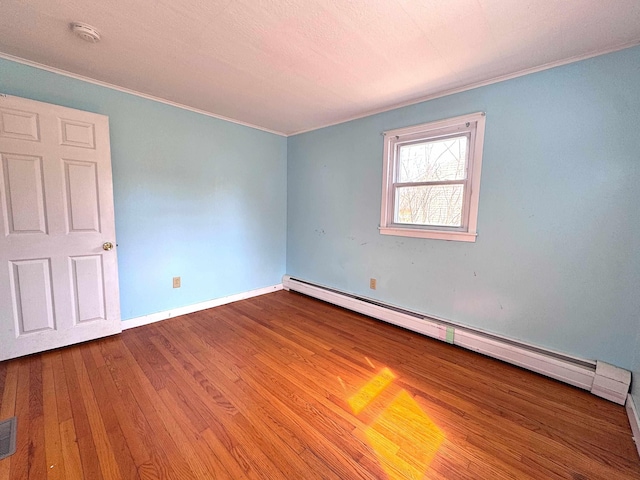 empty room with visible vents, baseboards, ornamental molding, baseboard heating, and wood finished floors