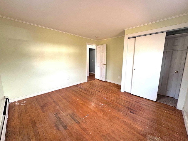 unfurnished bedroom with a closet, baseboards, ornamental molding, a baseboard heating unit, and wood-type flooring