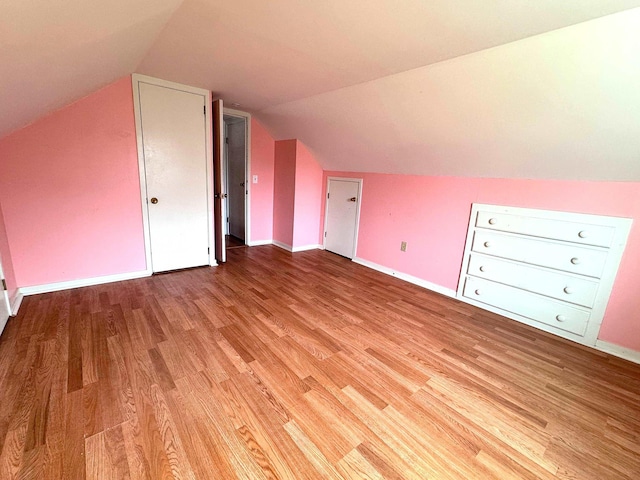 additional living space featuring light wood finished floors, baseboards, and vaulted ceiling