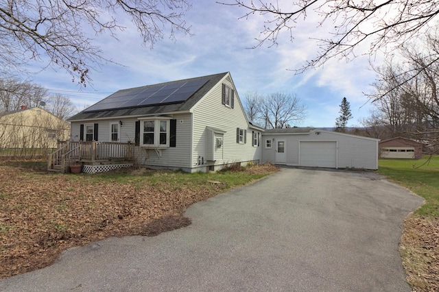 view of front of property with a deck, roof mounted solar panels, an attached garage, a shingled roof, and driveway