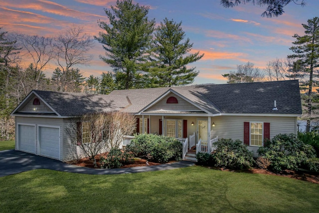 view of front facade with a yard, covered porch, an attached garage, a shingled roof, and driveway