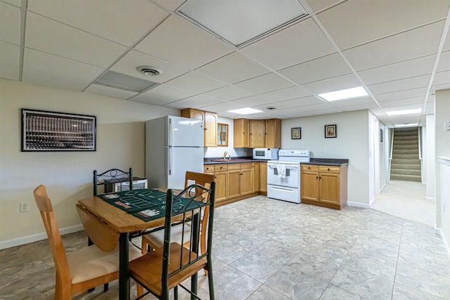 kitchen with a paneled ceiling, a sink, dark countertops, and white appliances