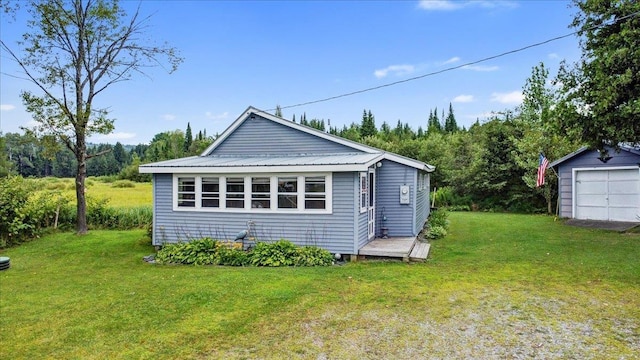 rear view of house with metal roof, a detached garage, an outdoor structure, and a lawn