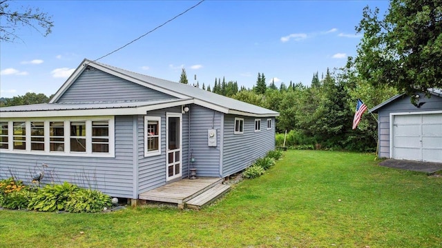 rear view of house with an outbuilding, a detached garage, metal roof, and a lawn
