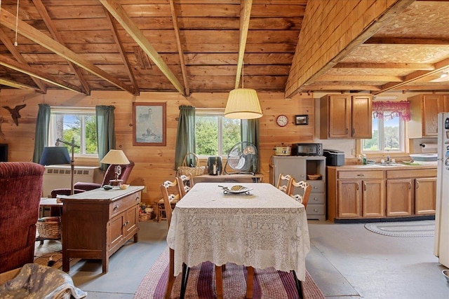 dining space with concrete floors, wood walls, beam ceiling, and plenty of natural light
