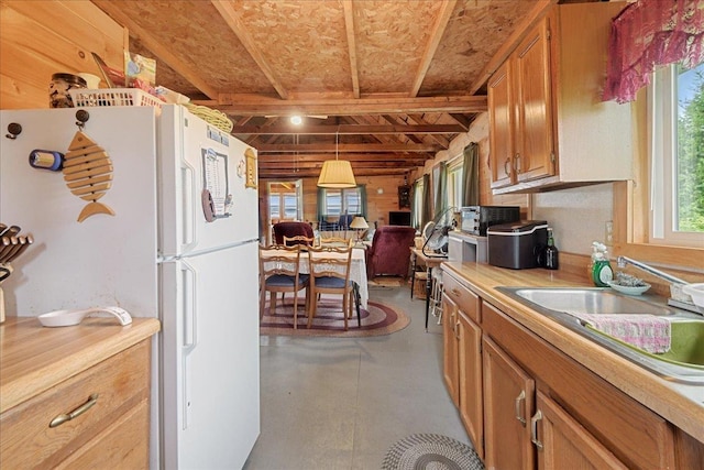 kitchen featuring finished concrete flooring, freestanding refrigerator, a sink, light countertops, and brown cabinets