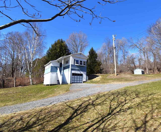 view of side of property featuring driveway, an attached garage, an outbuilding, a yard, and a storage unit