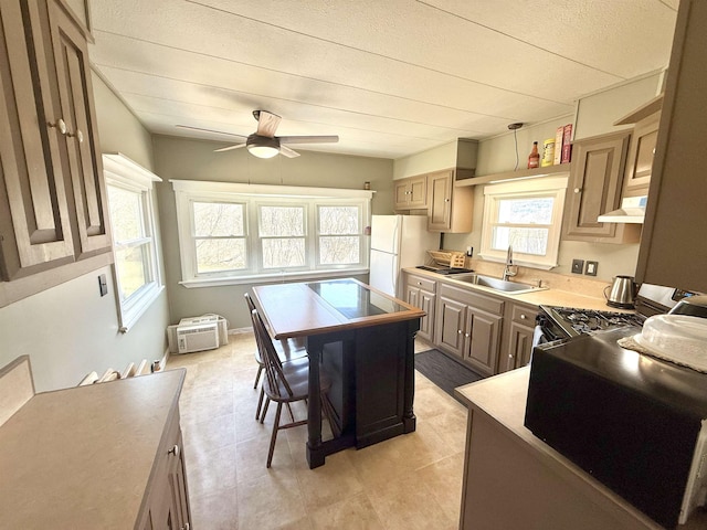 kitchen featuring freestanding refrigerator, a ceiling fan, gas range, under cabinet range hood, and a sink