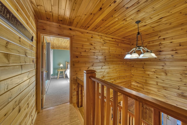 hall featuring a notable chandelier, an upstairs landing, wood walls, wood ceiling, and a baseboard radiator
