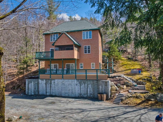 rear view of property featuring stairs, a balcony, and a shingled roof