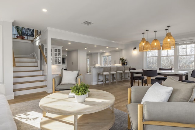 living area featuring a wealth of natural light, stairway, light wood-style flooring, and ornamental molding