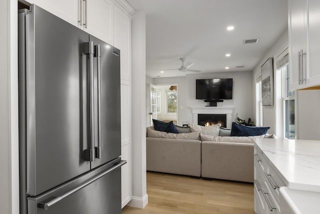 kitchen with a warm lit fireplace, a ceiling fan, white cabinets, visible vents, and high quality fridge