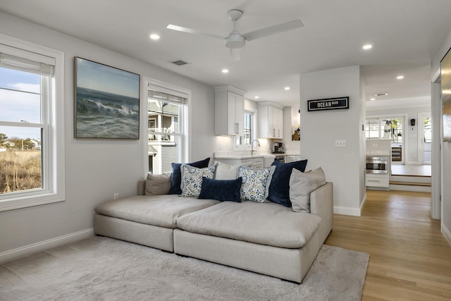 living room featuring a wealth of natural light, light wood-style floors, baseboards, and ceiling fan