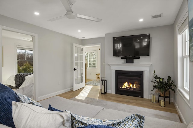 living room with visible vents, baseboards, ceiling fan, wood finished floors, and a glass covered fireplace
