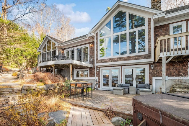 rear view of property featuring a hot tub, a chimney, a balcony, french doors, and a deck