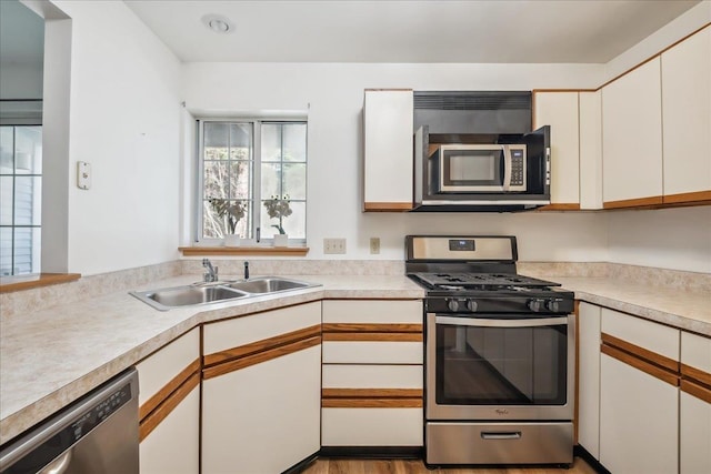 kitchen featuring appliances with stainless steel finishes, a sink, white cabinetry, and light countertops