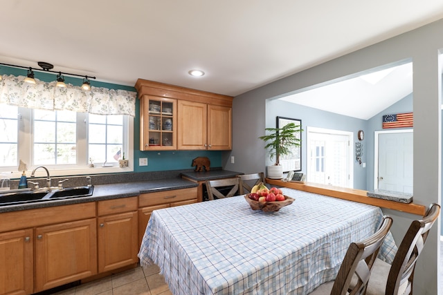 kitchen featuring a sink, glass insert cabinets, brown cabinetry, dark countertops, and lofted ceiling