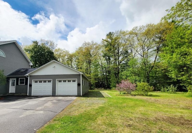 view of grassy yard featuring a garage and asphalt driveway