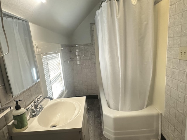 bathroom featuring lofted ceiling, vanity, shower / bath combo with shower curtain, and tile walls