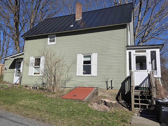rear view of property with a standing seam roof, a lawn, a chimney, and metal roof