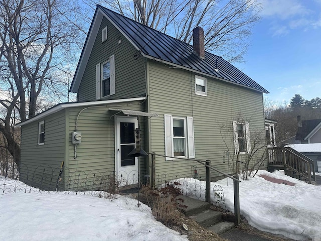view of snow covered exterior with a chimney, a standing seam roof, and metal roof