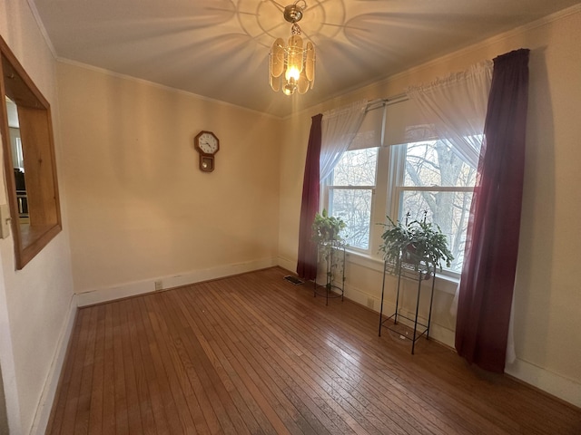 spare room with crown molding, hardwood / wood-style floors, a chandelier, baseboards, and visible vents
