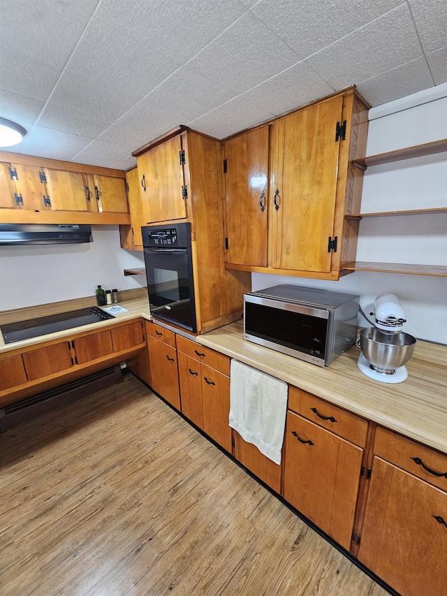 kitchen with light wood finished floors, open shelves, brown cabinetry, light countertops, and black appliances