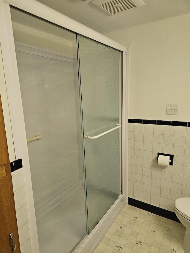 bathroom featuring toilet, tile walls, tile patterned floors, and a stall shower
