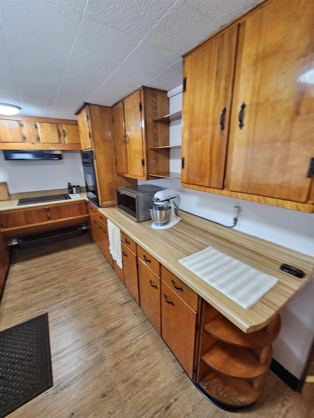 kitchen with open shelves, brown cabinetry, black appliances, light wood-style flooring, and light countertops