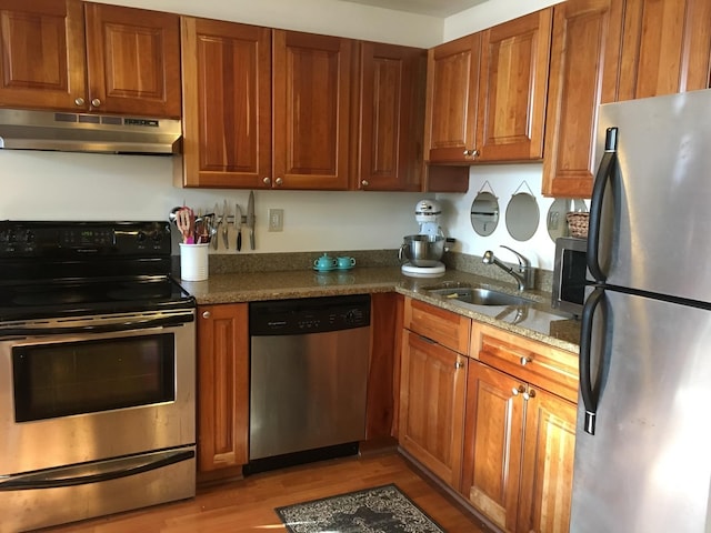 kitchen featuring appliances with stainless steel finishes, under cabinet range hood, a sink, light wood-style flooring, and brown cabinetry