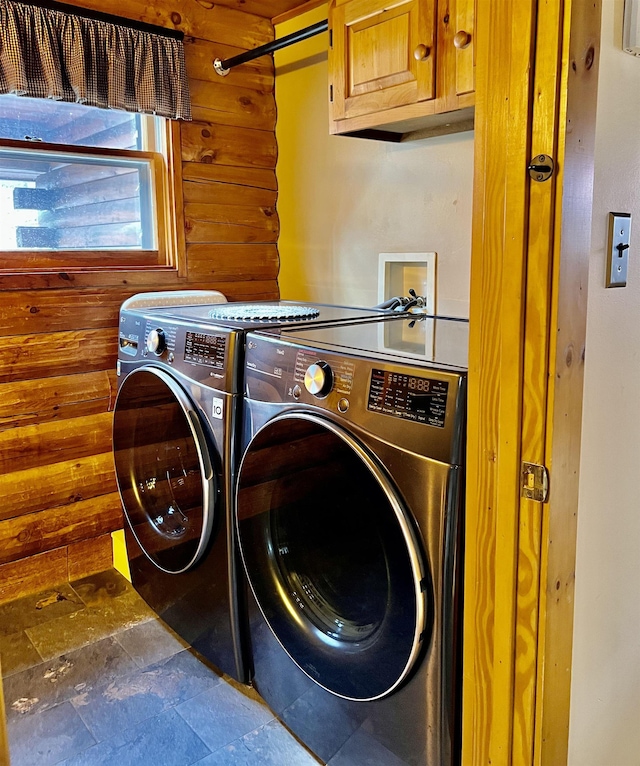 clothes washing area featuring washer and dryer, wood walls, cabinet space, and stone finish floor