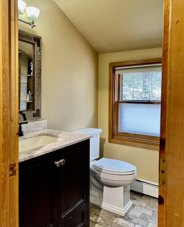 bathroom with a baseboard radiator, stone finish floor, toilet, and vanity
