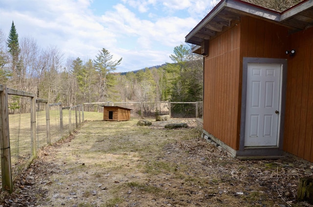 view of yard with fence, an outdoor structure, and a forest view