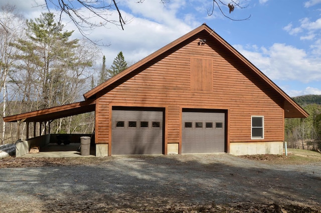 view of property exterior featuring a garage, log veneer siding, driveway, and an outdoor structure