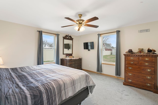 bedroom featuring light colored carpet, baseboards, a ceiling fan, and multiple windows