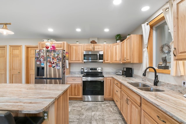 kitchen with light stone countertops, stainless steel appliances, light brown cabinetry, and a sink