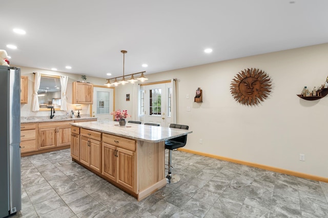 kitchen featuring light brown cabinets, a sink, a breakfast bar area, freestanding refrigerator, and a kitchen island