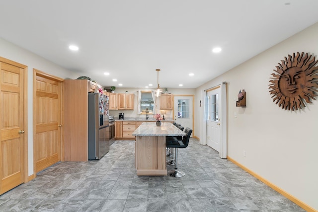 kitchen with a center island, light brown cabinetry, stainless steel fridge, a kitchen bar, and baseboards