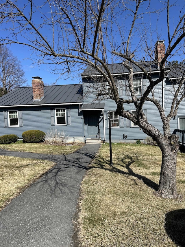 view of front of property featuring a front lawn, aphalt driveway, a chimney, a standing seam roof, and metal roof