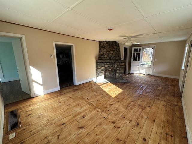 unfurnished living room featuring a stone fireplace, visible vents, a ceiling fan, wood-type flooring, and baseboards