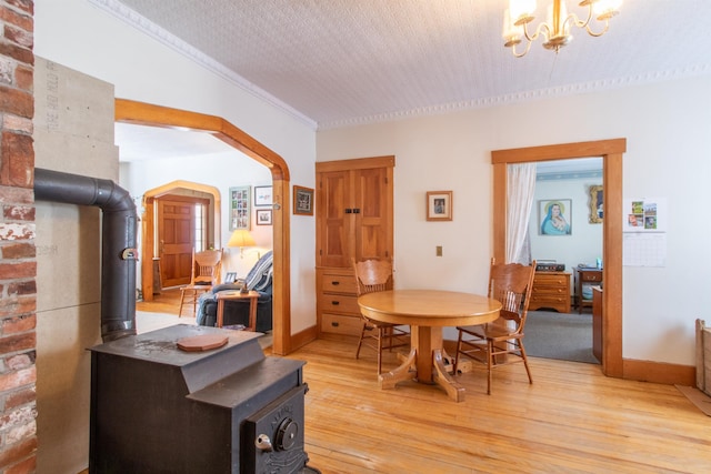dining room with light wood-style flooring, arched walkways, a chandelier, and a wood stove