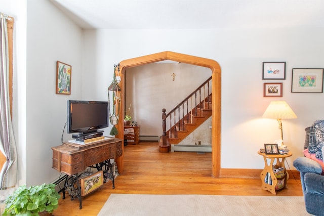 living area with baseboard heating, wood finished floors, and stairs