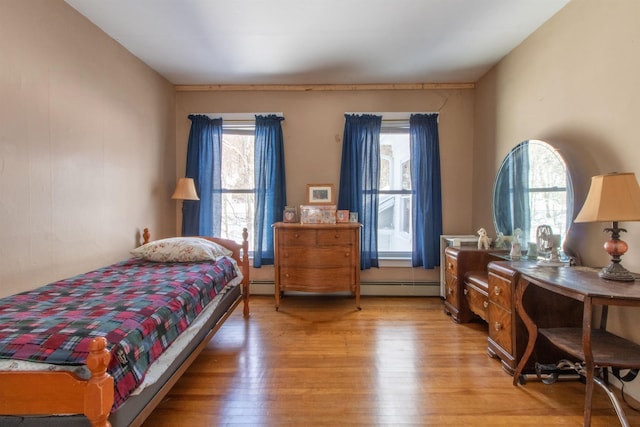 bedroom with a baseboard heating unit, light wood finished floors, and multiple windows