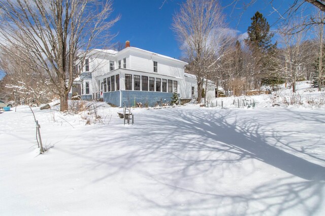 view of snow covered exterior featuring a chimney and a sunroom
