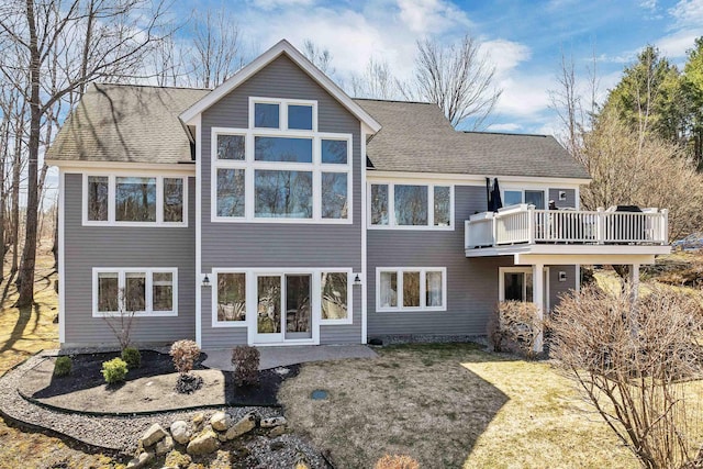 back of property with a wooden deck, roof with shingles, and a yard